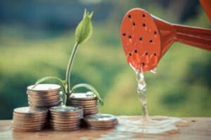 Pre-seed funding concept. Piles of coins being watered by red watering can sprouting plant