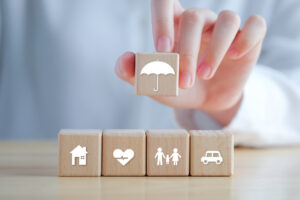 Insurance concept. Protection against a possible eventuality. Hand holding umbrella icon and House, Car, Family and Health icon on wooden block for assurance life concept